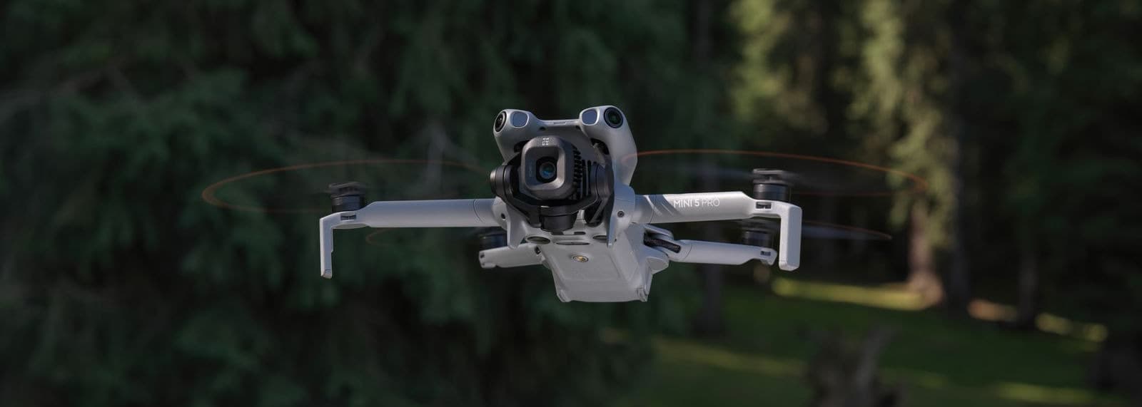 En drönare svävar i luften framför en skog, redo att fånga naturens skönhet från ovan.