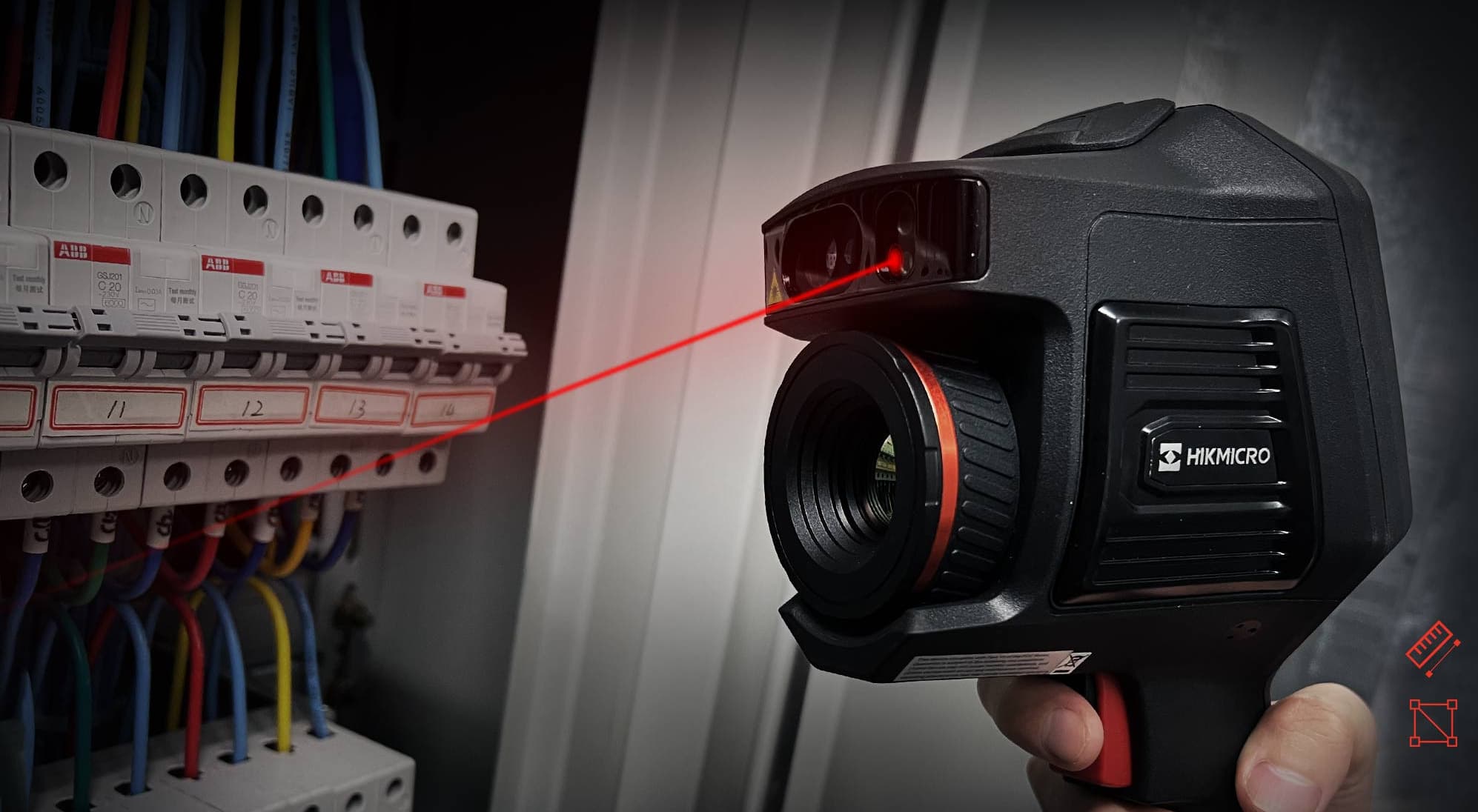 En handhållen termisk kamera riktas mot en elektrisk panel, med en röd laser som pekar på brytarna för precisionsmätning.