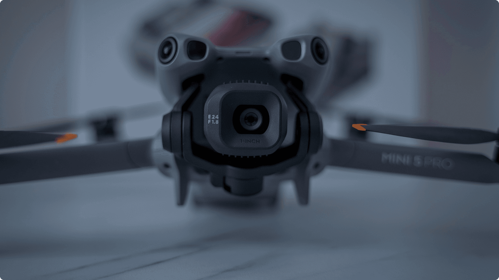 En närbild av en DJI Mini 5 Pro-drönare med fokus på dess kamera och propellrar, placerad på en slät yta.