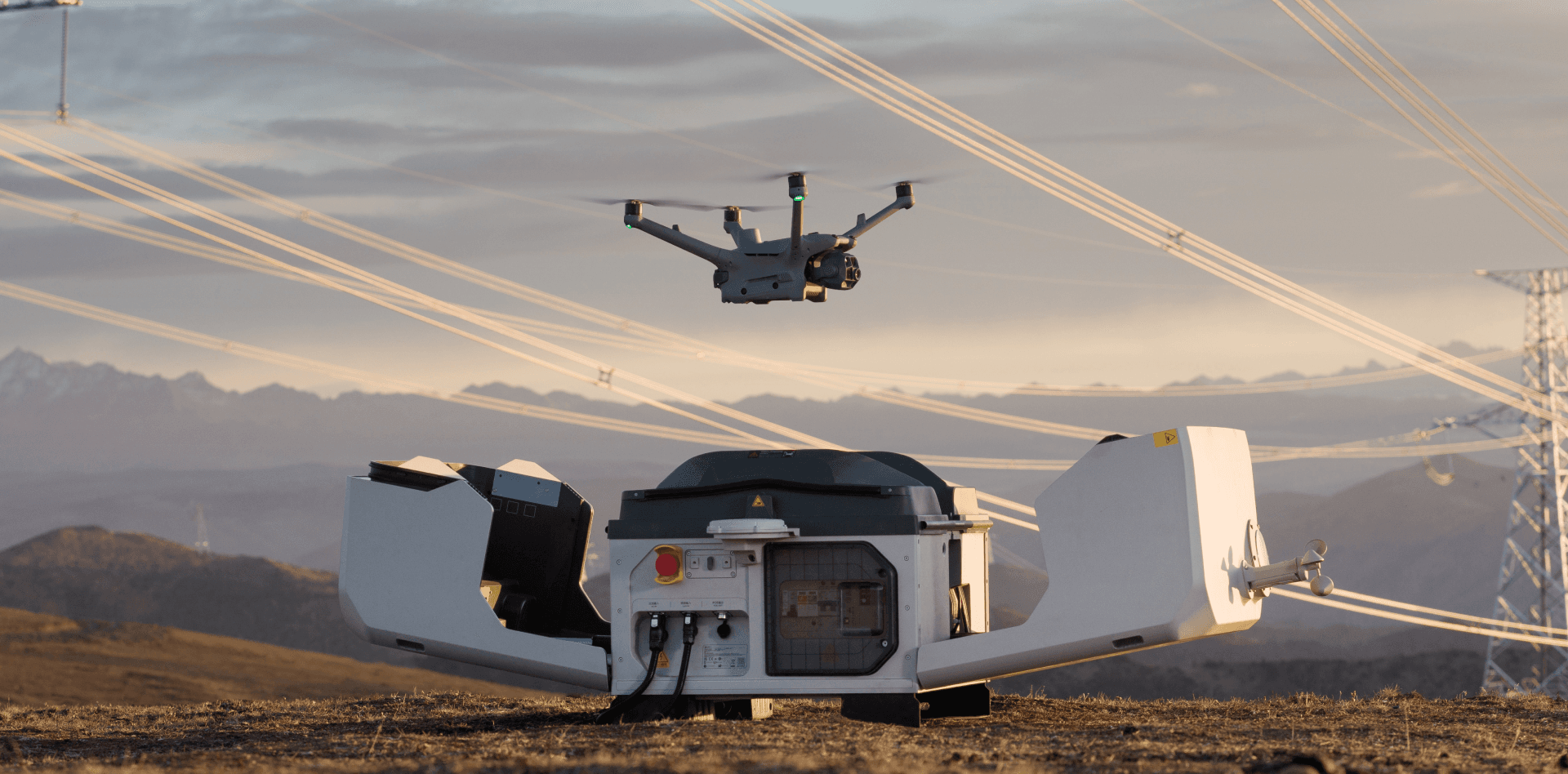 En drönare lyfter från en landningsstation i ett öppet landskap med kraftledningar i bakgrunden.