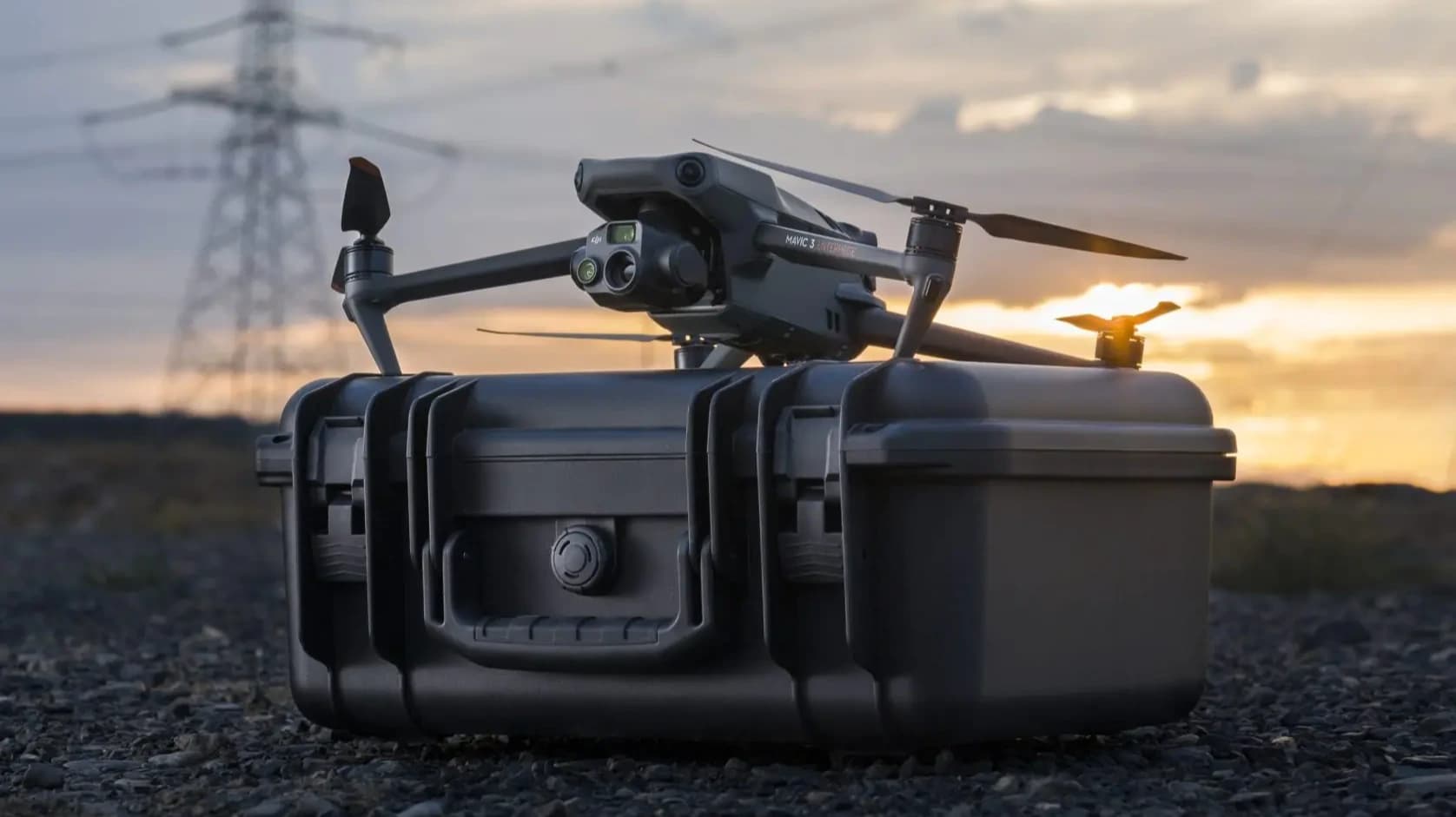 En DJI Mavic 3 Thermal Advanced (M3TA) vilar på en robust transportväska vid solnedgången, med kraftledningar i bakgrunden.
