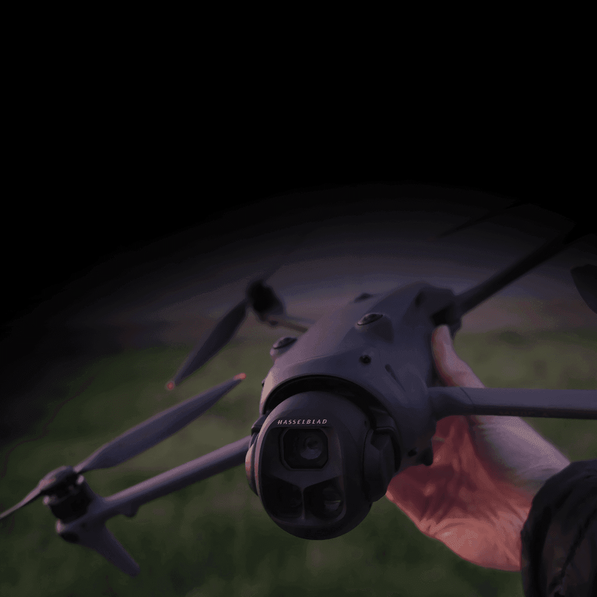 En hand håller en avancerad drönare med en kamera, redo för flygning över ett grönskande landskap.