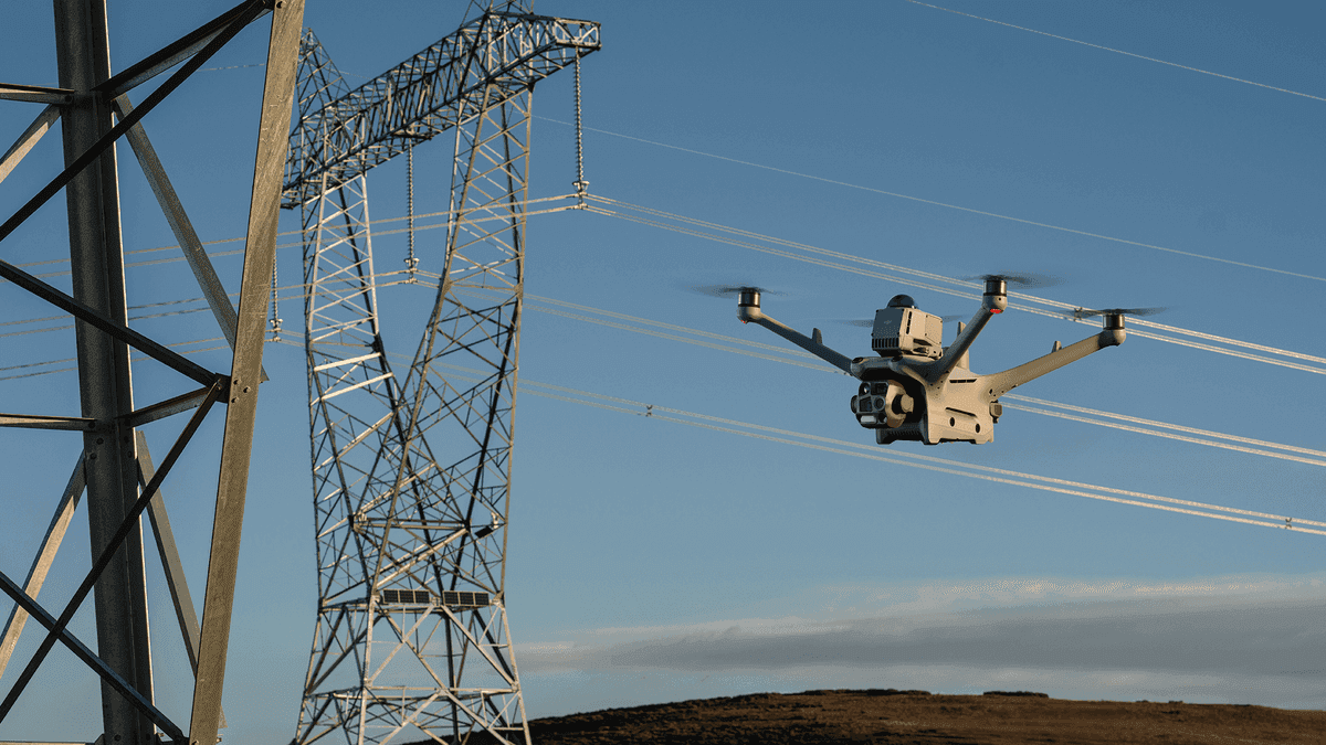 En drönare inspekterar kraftledningar vid en högspänningsmast under en klar himmel.