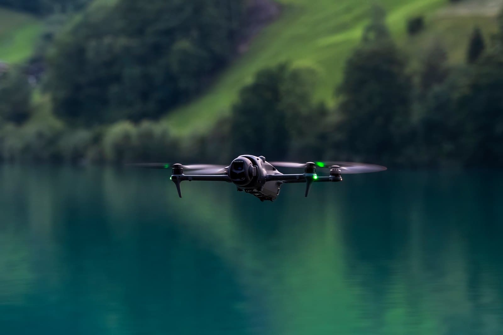 En DJI Mavic 4 Pro-drönare svävar över en stilla sjö med en grönskande skog i bakgrunden.