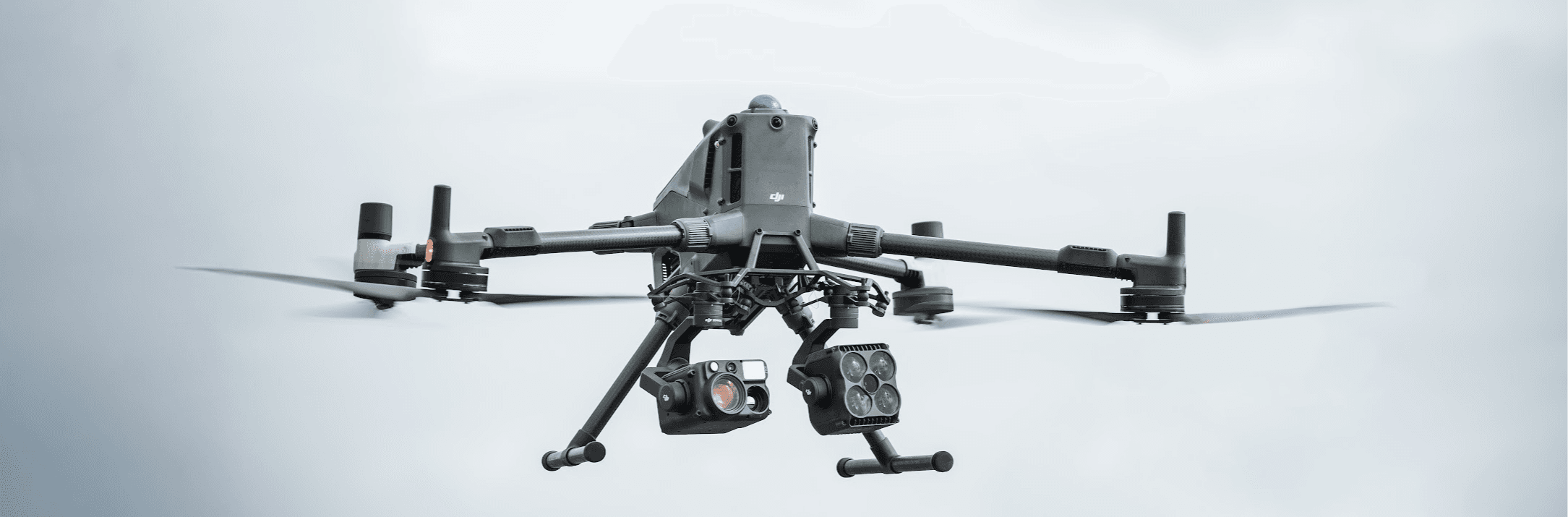 En DJI Matrice 400 drönare svävar i luften mot en molnig himmel, utrustad med flera sensorer och kameror.