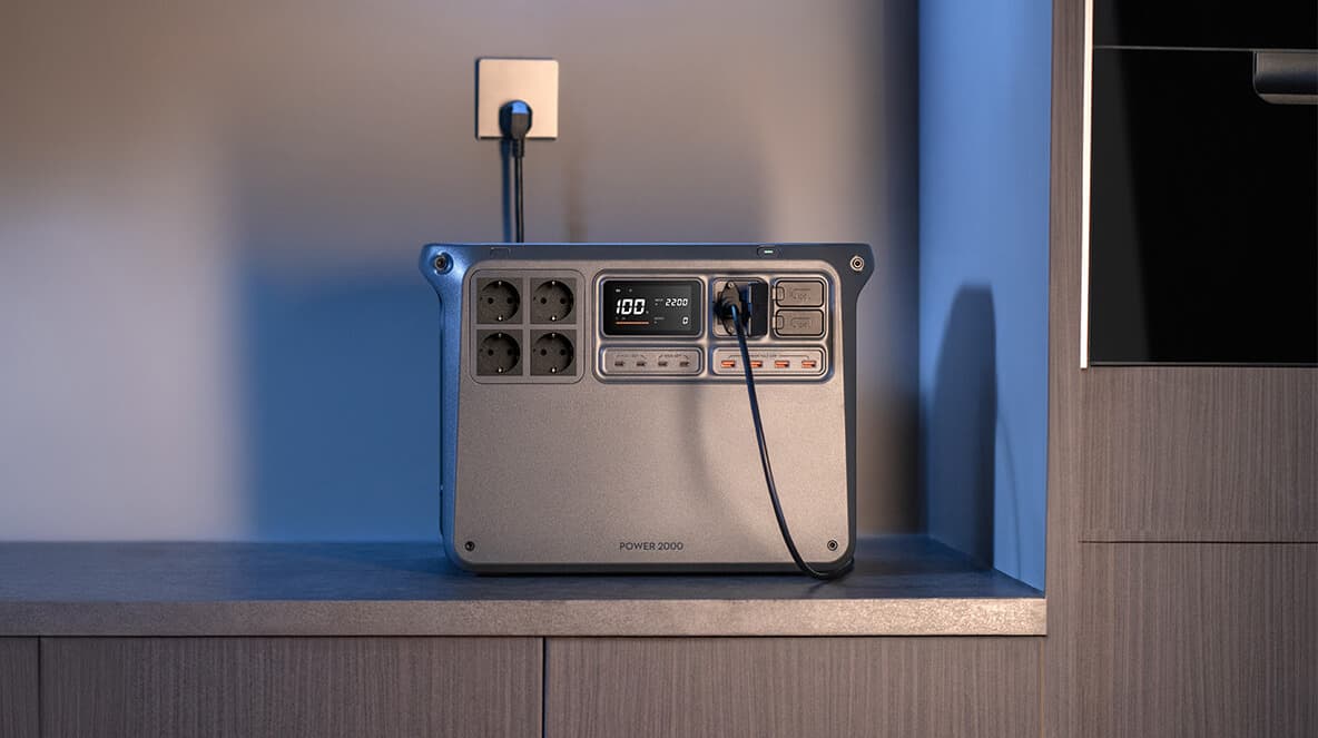 En kraftfull bärbar DJI Power 2000 placerad på en hylla, ansluten till ett vägguttag, med digital display som visar laddningsstatus.