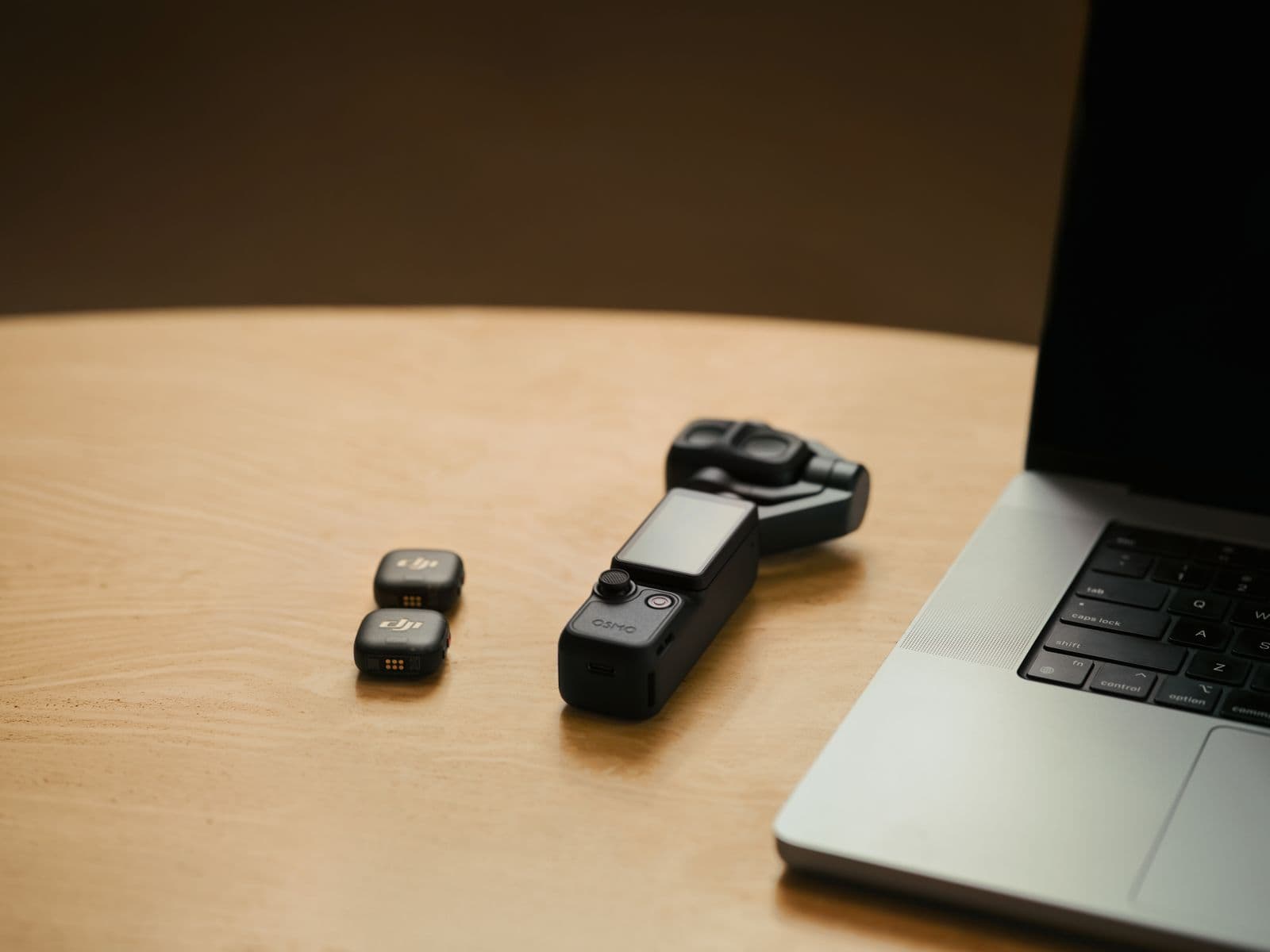 DJI Osmo Pocket 4P och två DJI Mic Mini-sändare på ett träskrivbord bredvid en bärbar dator.