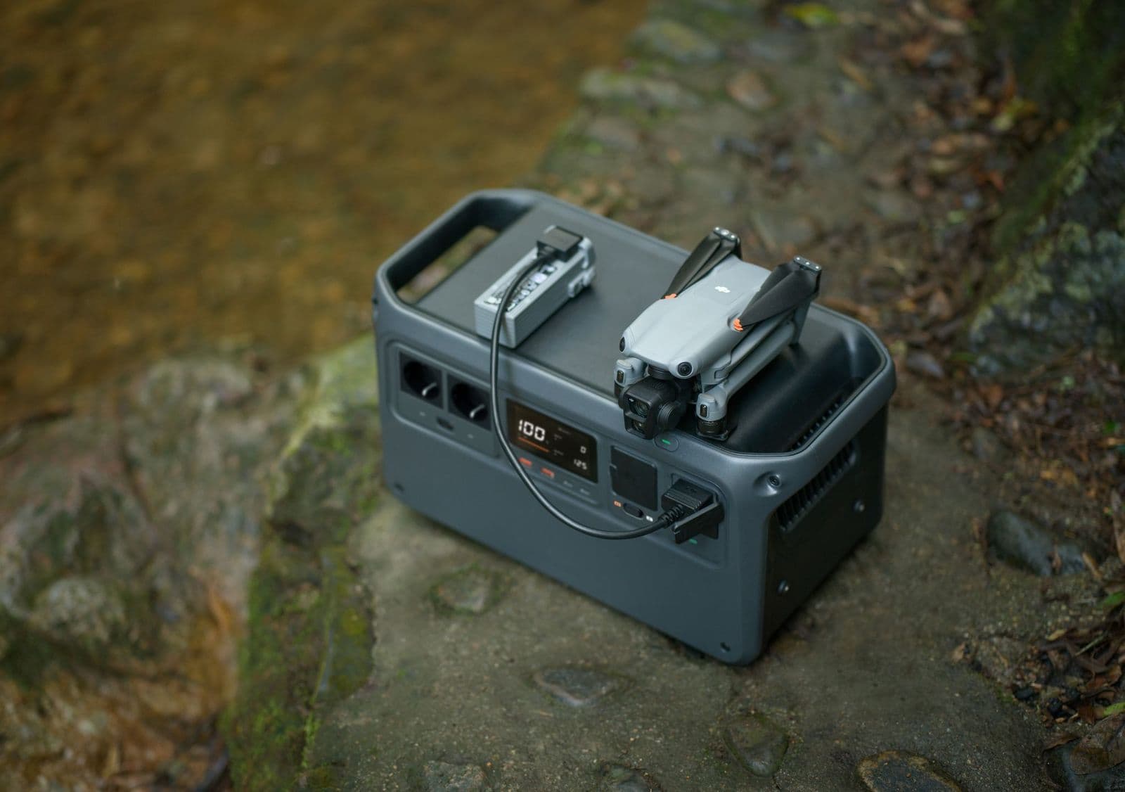 En hopfälld drönare laddas på en bärbar DJI Power 1000 V2-kraftstation vid en stenig bäck.