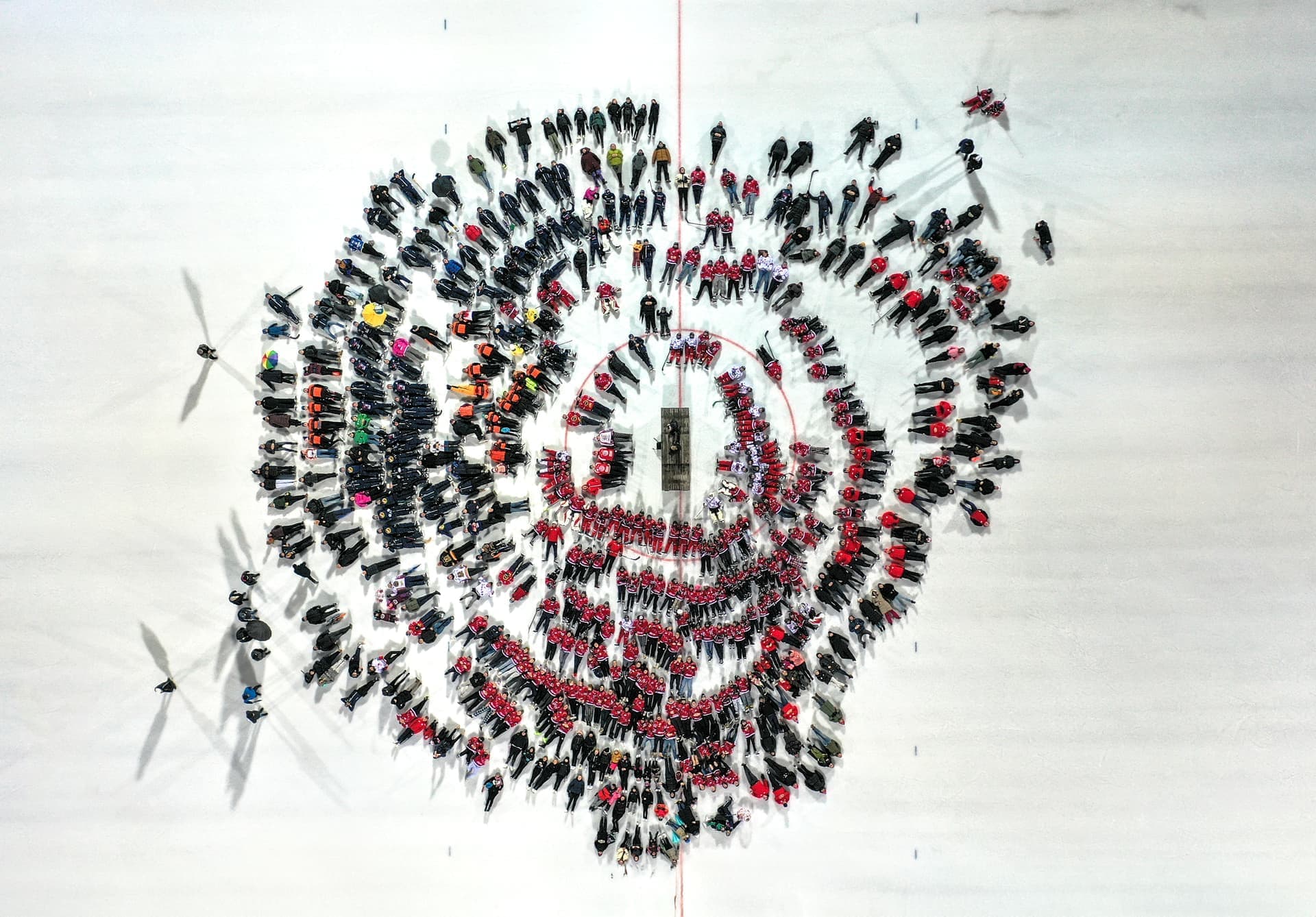 En stor grupp människor står i koncentriska cirklar på en isbana, sett från ovan.