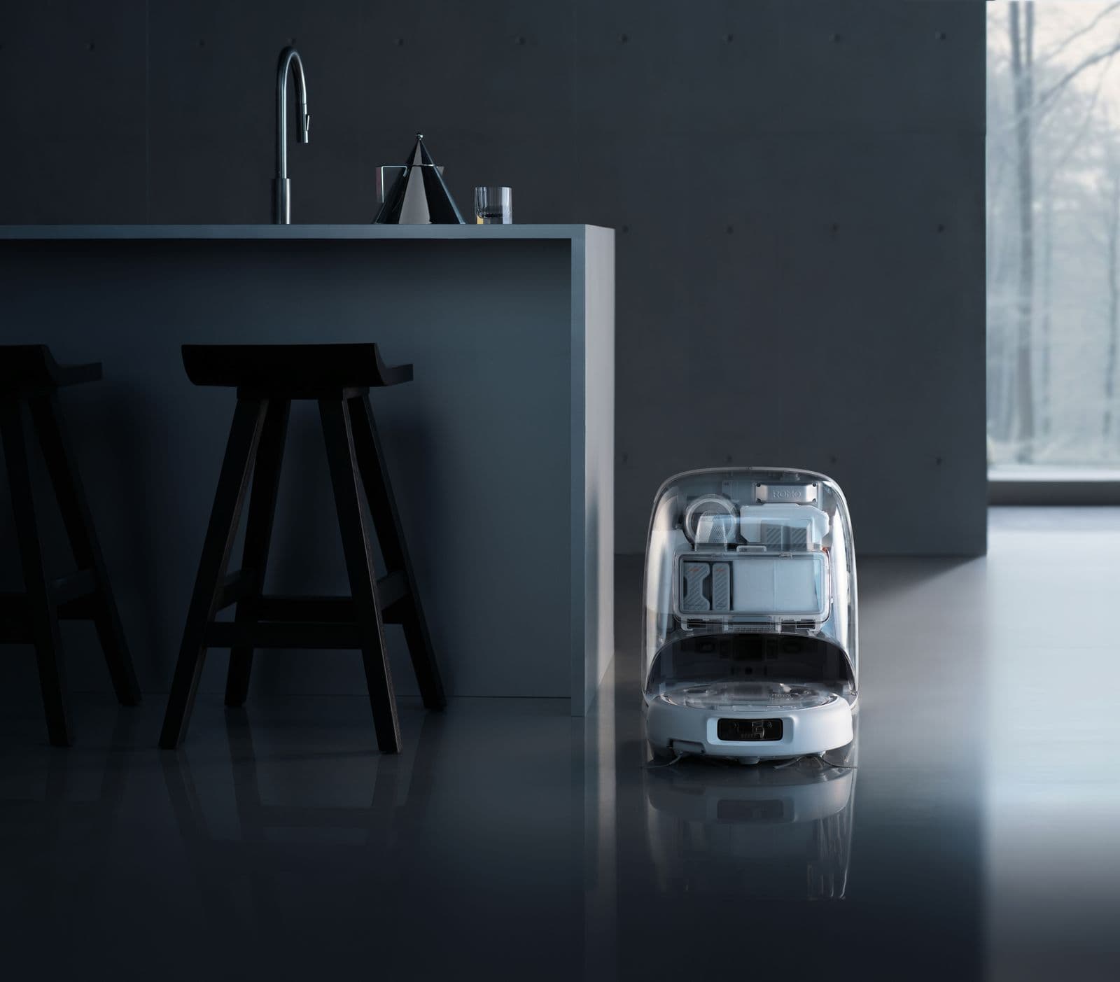 En kompakt robot med genomskinligt skal står vid en modern köksö i ett stilrent, minimalistiskt rum.
