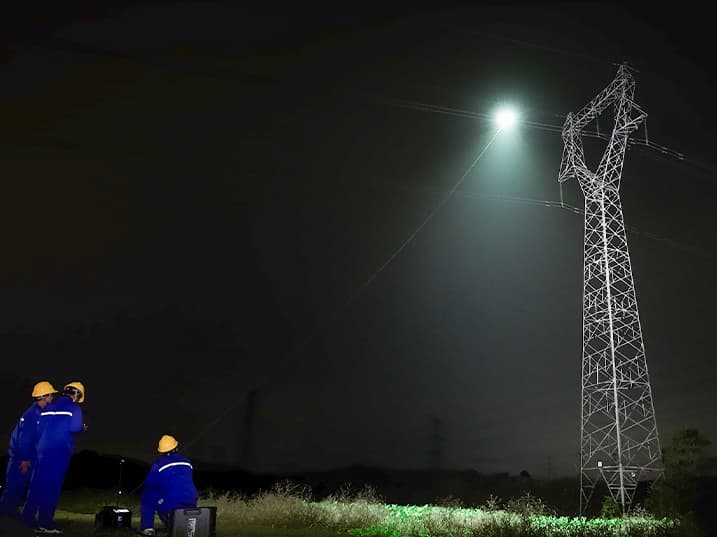 Tre arbetare i blå overaller som lyser upp en kraftledning med ML200 på en drönare.