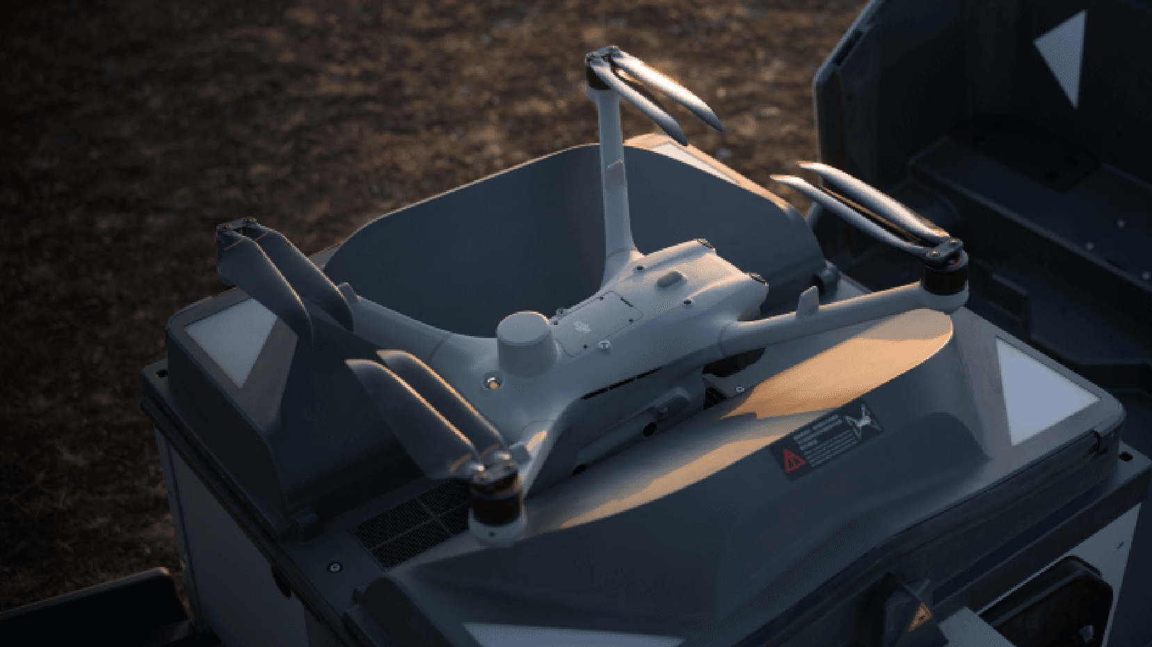 En drönare vilar på en landningsplattform i ett utomhusområde, belyst av mjukt kvällsljus.