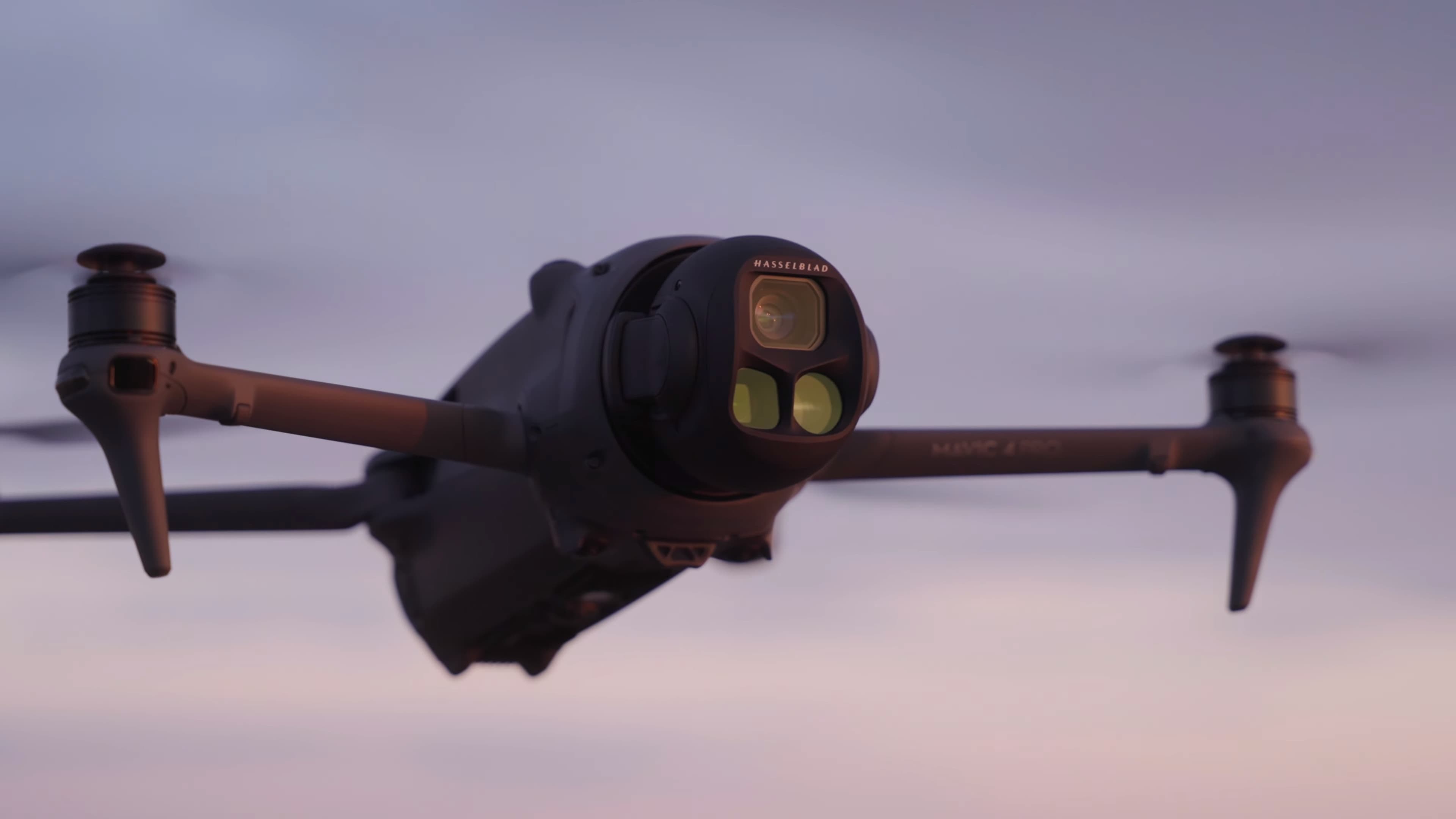 En drönare svävar i luften mot en mjukt färgad himmel, utrustad med avancerad kamerateknik.