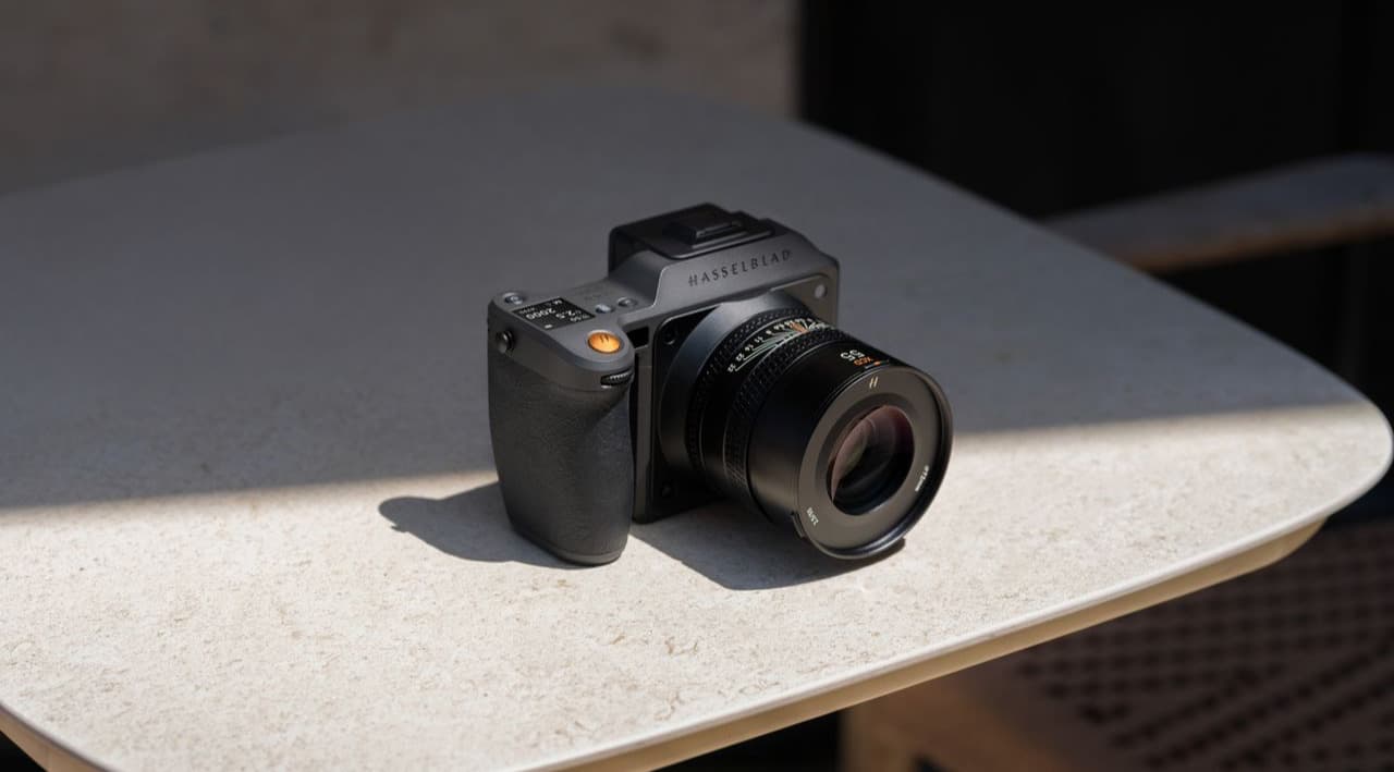 En modern Hasselblad X2D II 100C-kamera placerad på ett solbelyst bord, omgiven av skuggor.