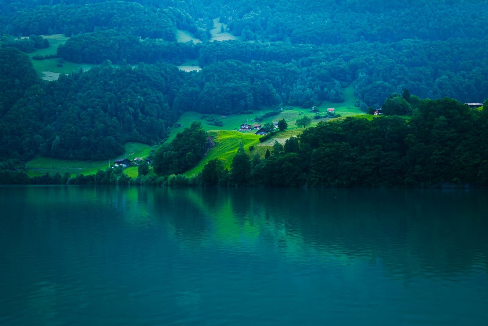 Drönarfoto taget med DJI Mavic 4 Pro: En lugn sjö reflekterar de frodiga gröna kullarna och skogarna i bakgrunden, med några hus utspridda på landskapet.