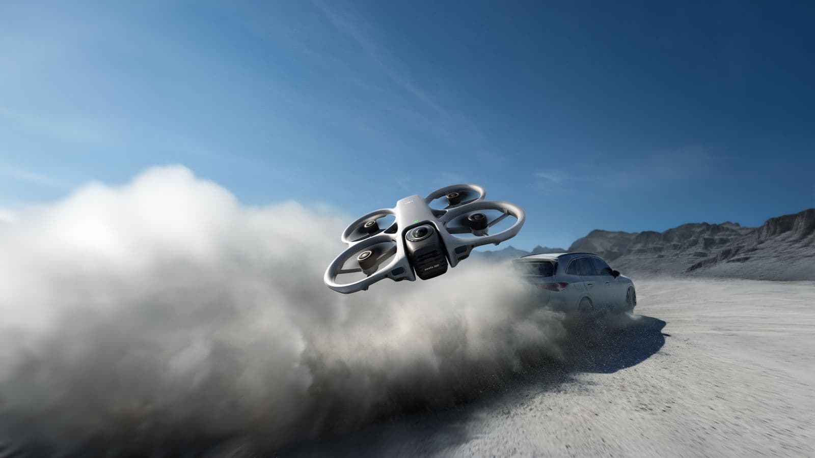 En DJI Avata 360-drönare svävar över en dammig väg medan en bil kör snabbt genom ett ökenlandskap.