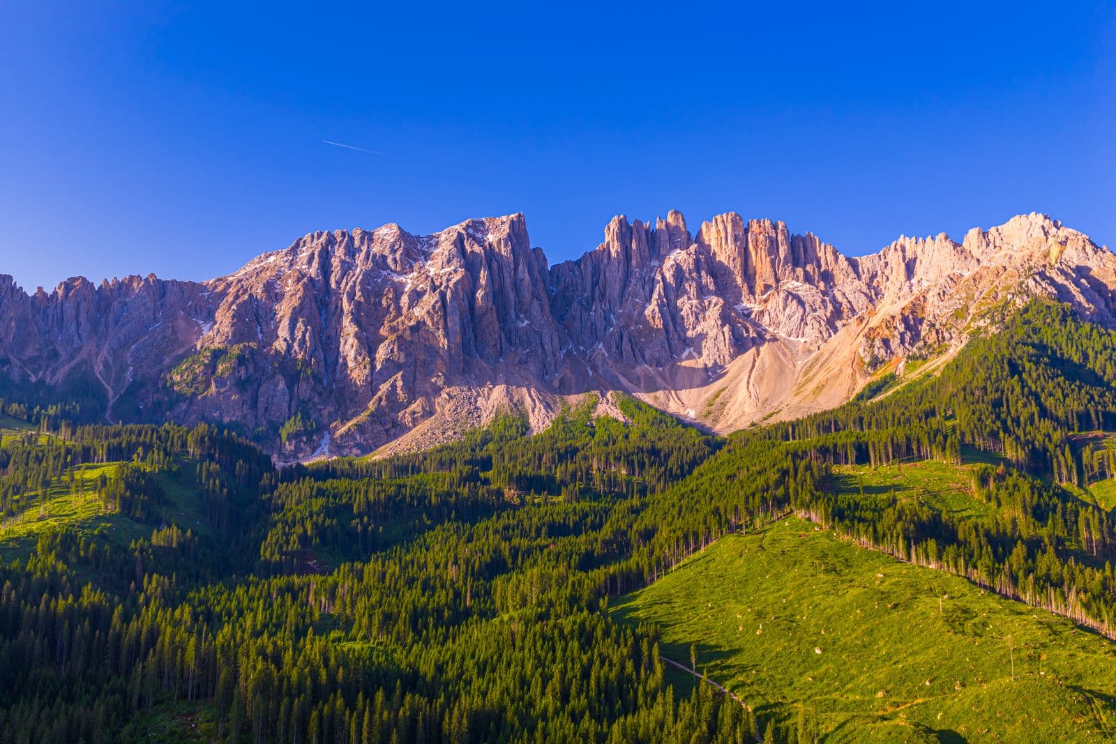 Drönarfoto taget med DJI Mavic 4 Pro: Majestätiska bergstoppar reser sig över en frodig granskog under en klarblå himmel.