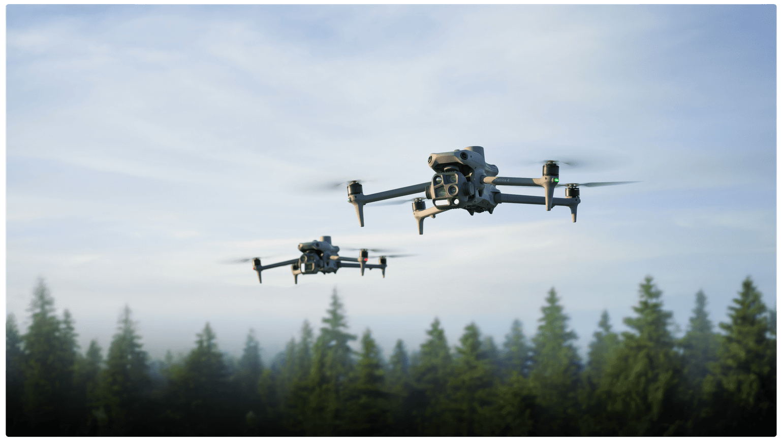 Två Matrice 4-drönare svävar över en skog, mot en klar himmel i bakgrunden.