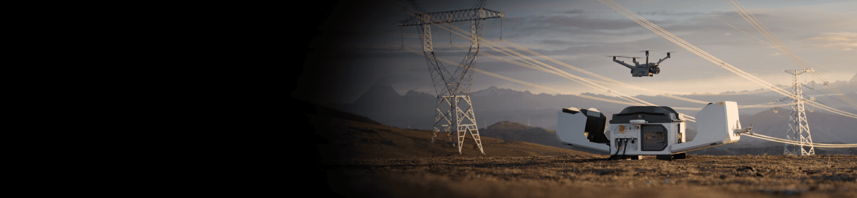 En drönare flyger nära kraftledningar i ett öppet landskap, med en landningsstation i förgrunden.