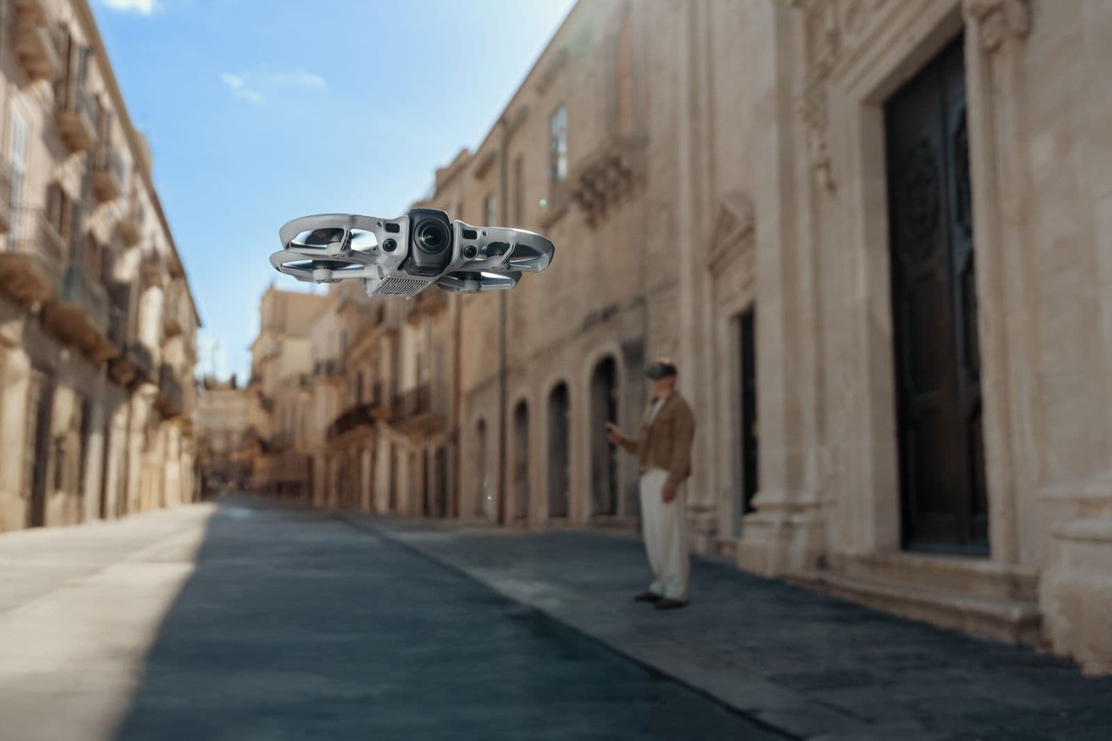 En DJI Avata 360-drönare svävar över en historisk gata medan en person i bakgrunden observerar.