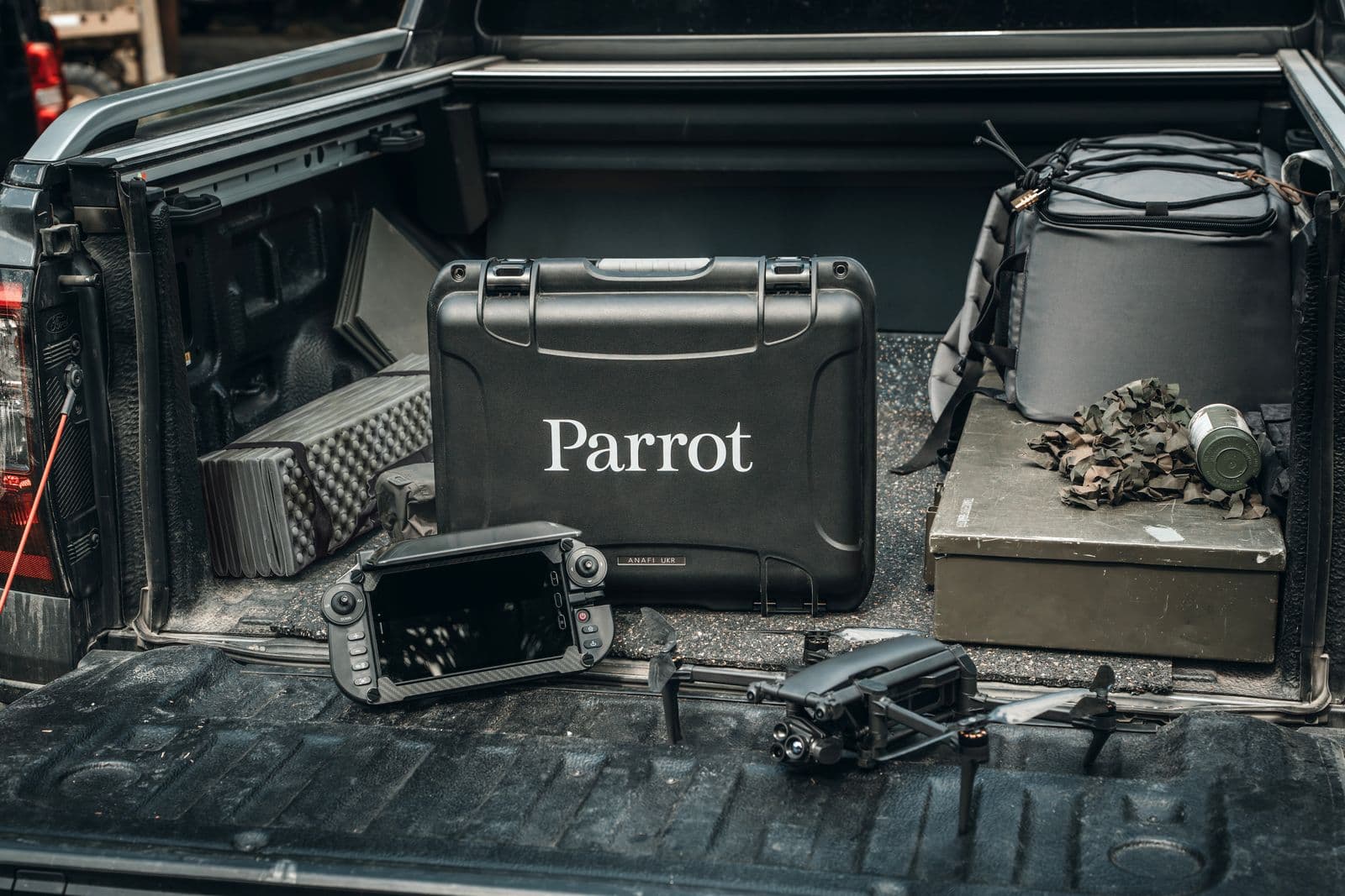 En drönare och en kontrollenhet ligger i bakluckan på ett fordon, omgivna av en robust väska märkt 'Parrot' och annan utrustning.