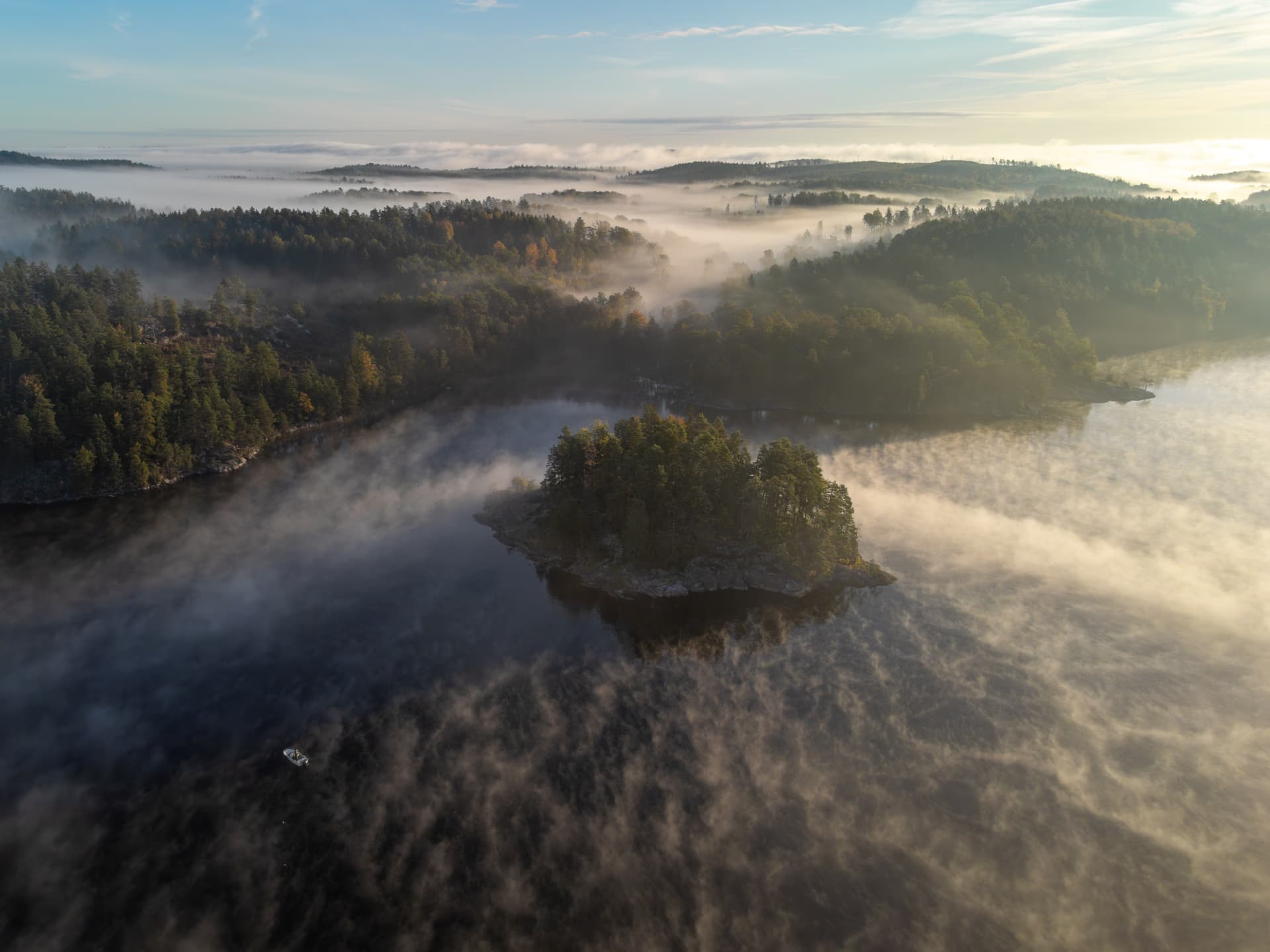 En dimtäckt skärgård med små öar omgivna av stilla vatten, badar i mjukt morgonljus.
