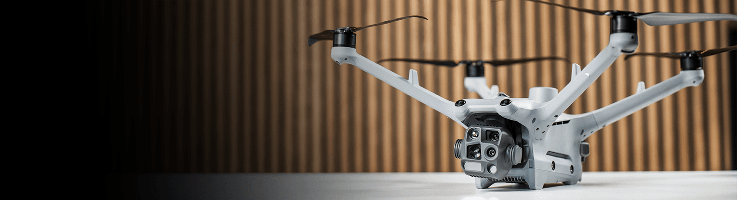 En DJI Matrice 4TD-drönare med flera kameror står på ett bord framför en träpanelvägg.