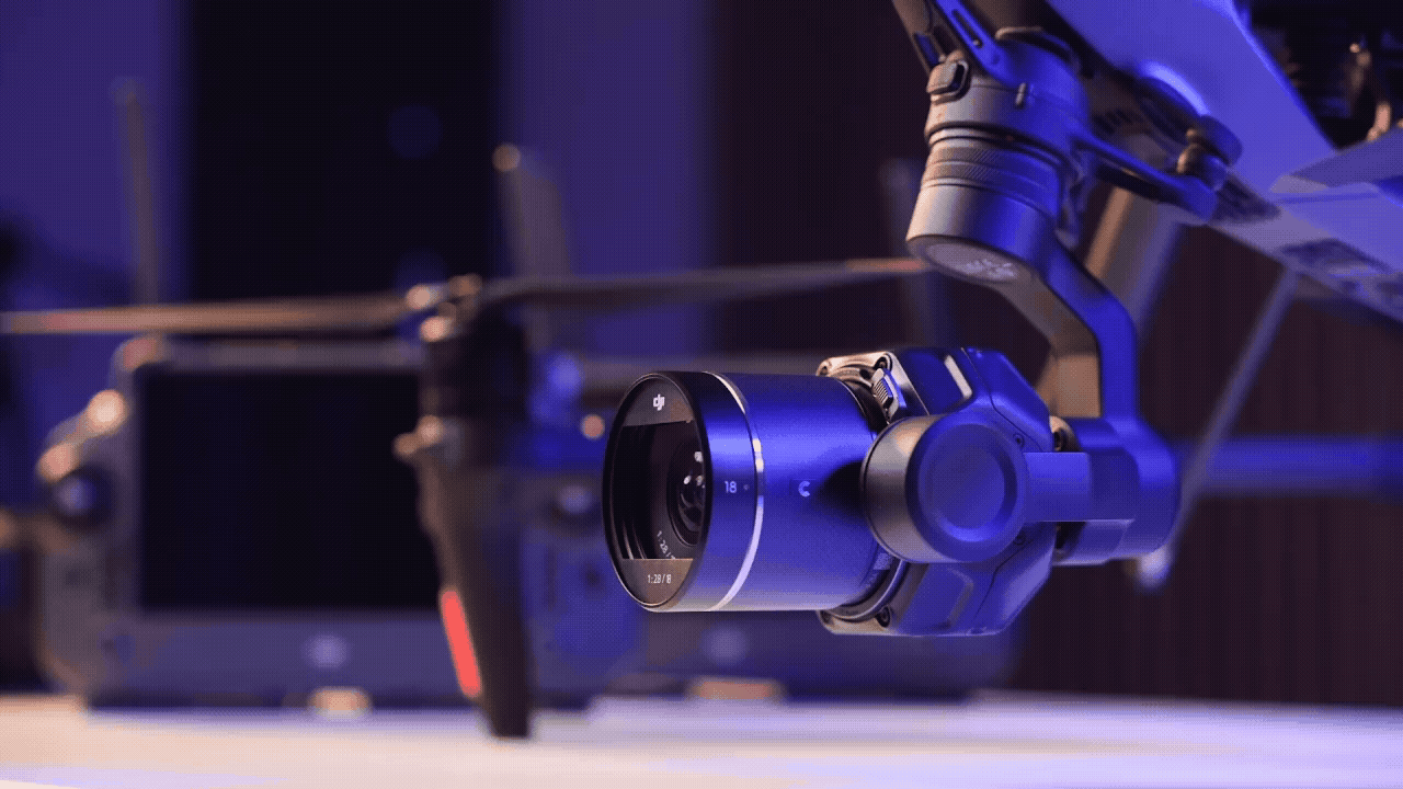 En närbild av en drönare utrustad med en avancerad kamera, belyst i ett blått sken, med en fjärrkontroll synlig i bakgrunden.