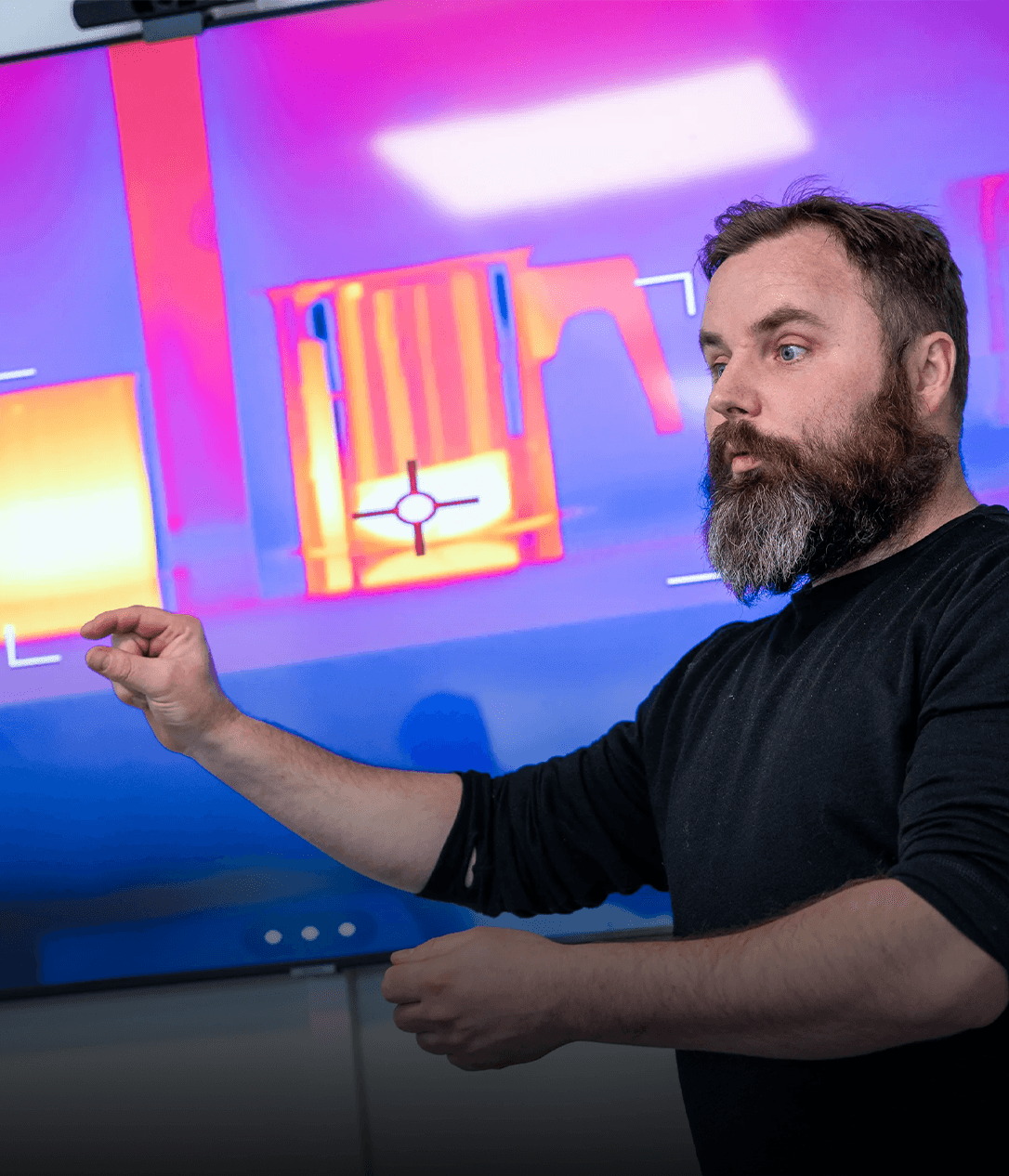 En person gestikulerar framför en skärm som visar en värmekarta i starka färger.