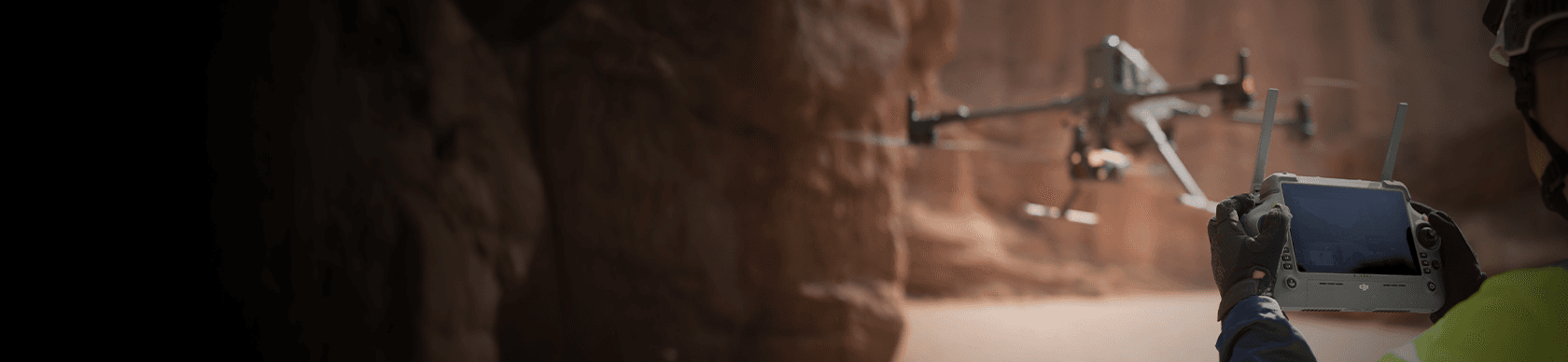 En person styr en drönare med en fjärrkontroll i en karg, stenig miljö.