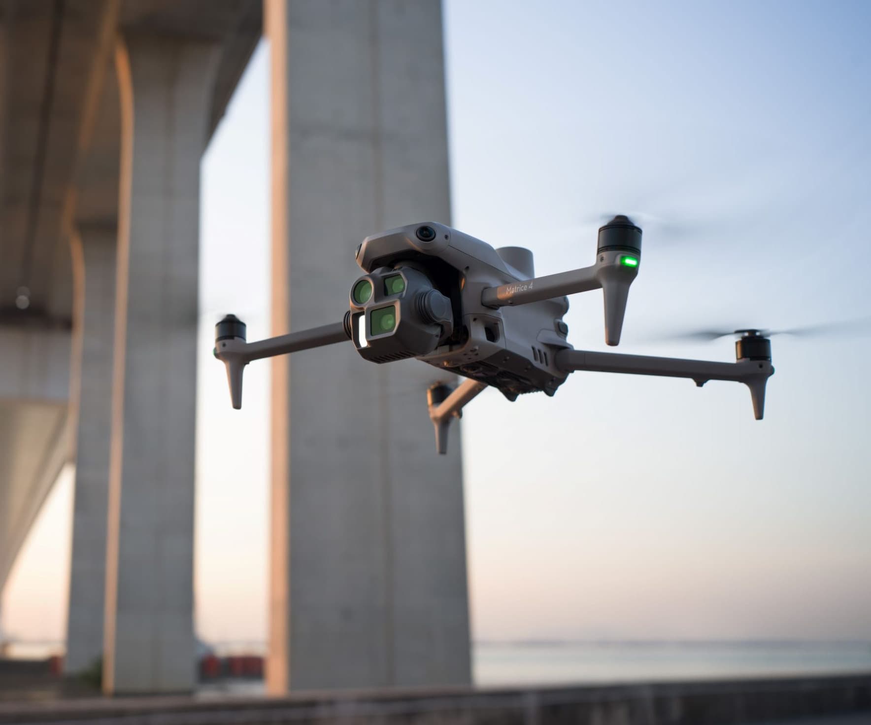 En drönare svävar framför en stor betongbro vid solnedgången, vilket skapar en futuristisk känsla.