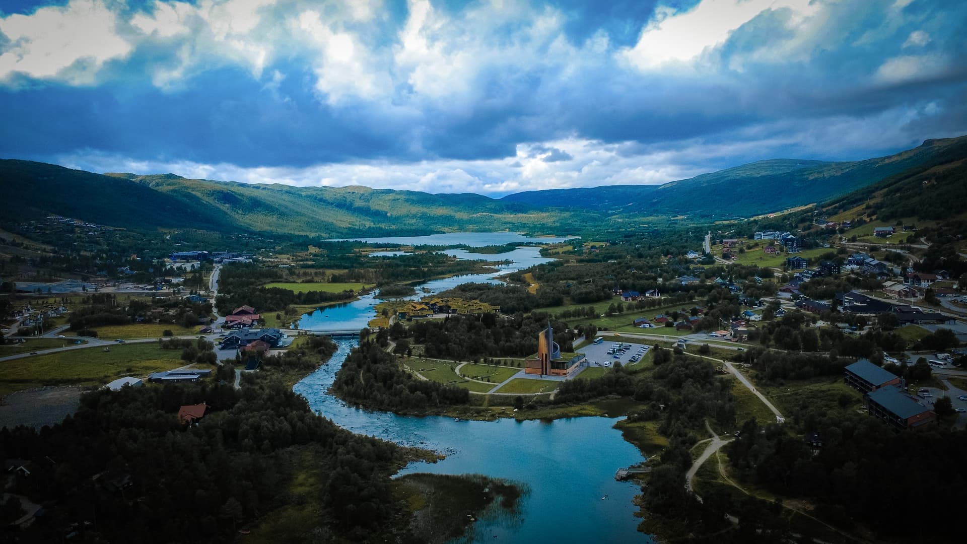 En naturskön dal med en slingrande flod och omgivande berg, där en kyrka står centralt i landskapet.