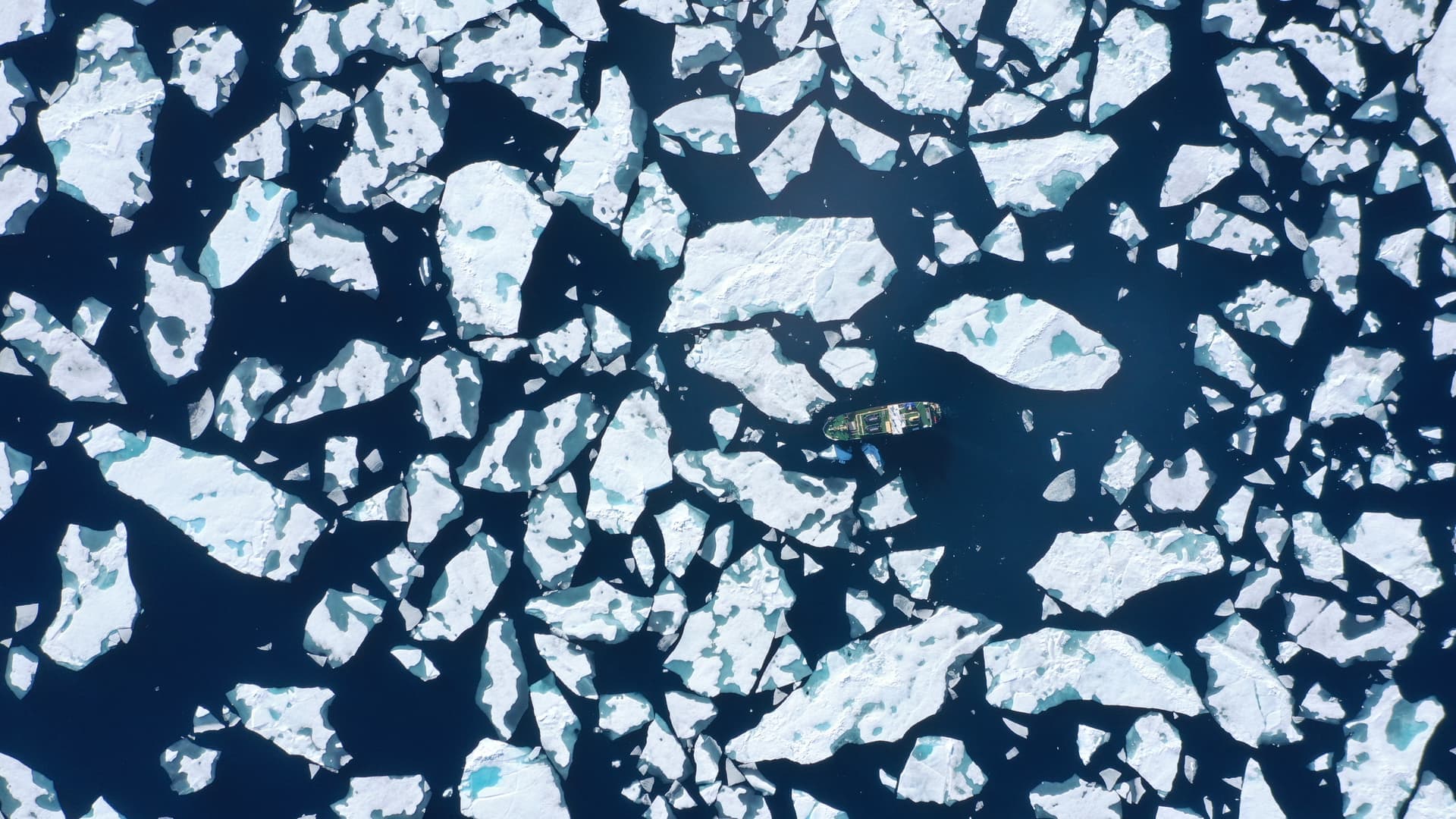 Ett fartyg navigerar genom ett hav av isflak i ett kallt, arktiskt landskap.