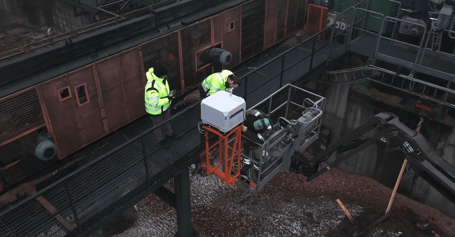 Två personer i varselkläder övervakar arbete med en maskin på en industriell anläggning.