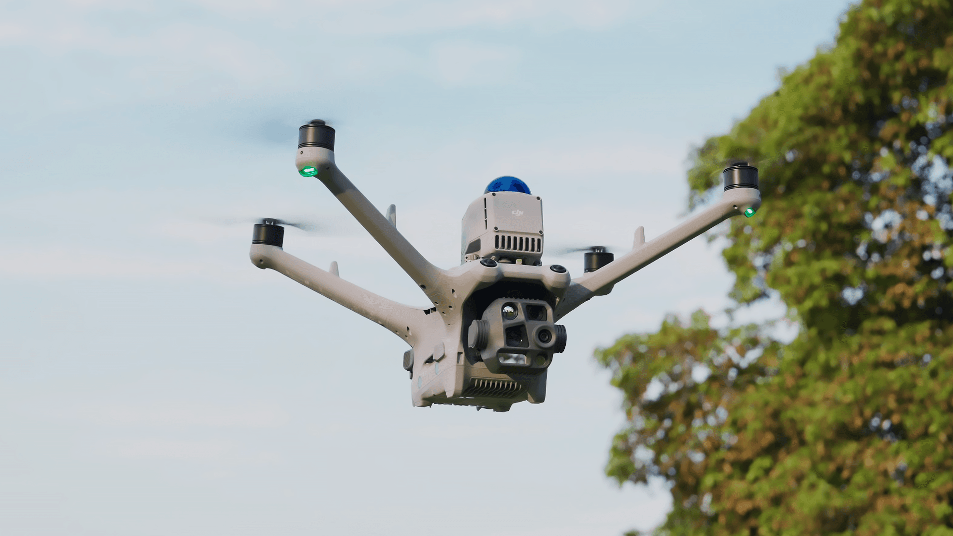 En avancerad drönare svävar i luften mot en klar himmel, med träd i bakgrunden.