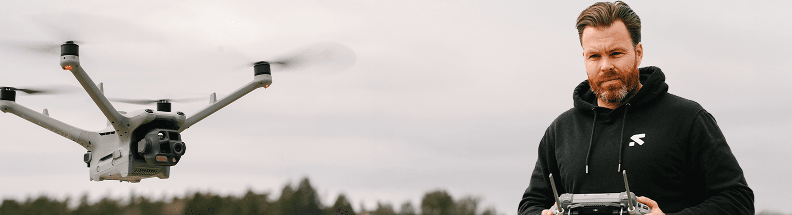 En person styr en avancerad drönare med en fjärrkontroll utomhus, mot en molnig himmel.